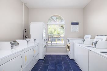 A laundry room with white washers and dryers and a window